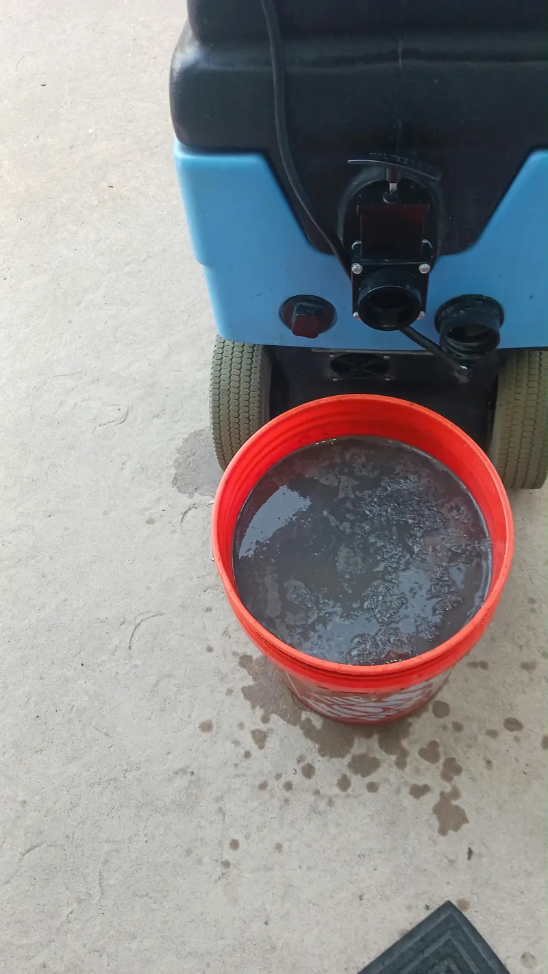 A bucket of dark rinse water beside an extraction machine on a carpet
