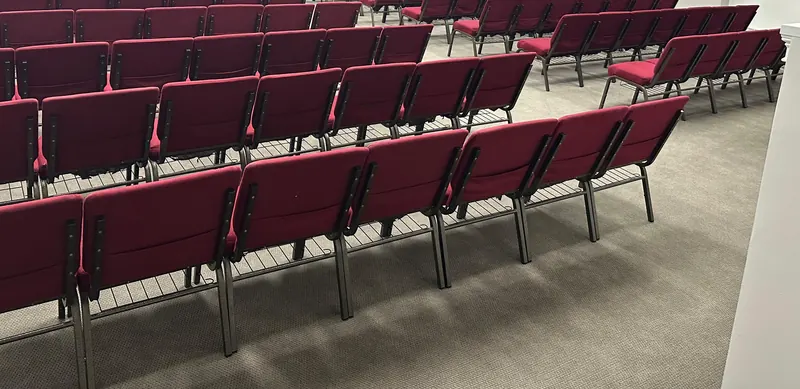 Rows of red upholstered chairs on a gray carpet in an assembly hall