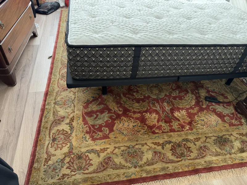 A quilted mattress on its base above a red and gold Oriental rug