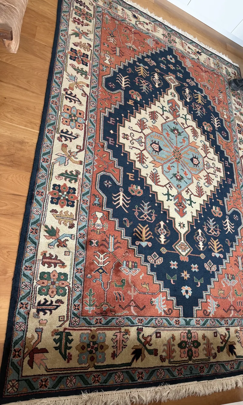 A hand knotted rug with a navy medallion on a coral field, laid on a hardwood floor