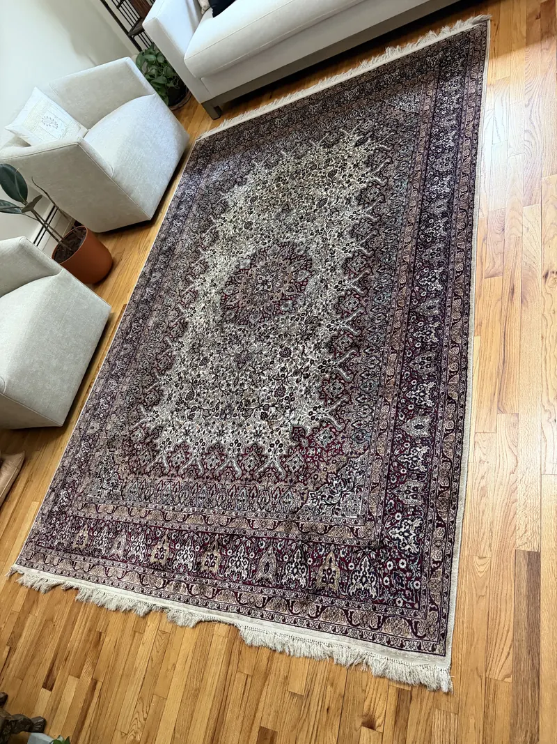 A finely patterned Persian style rug with ivory fringe on a hardwood floor