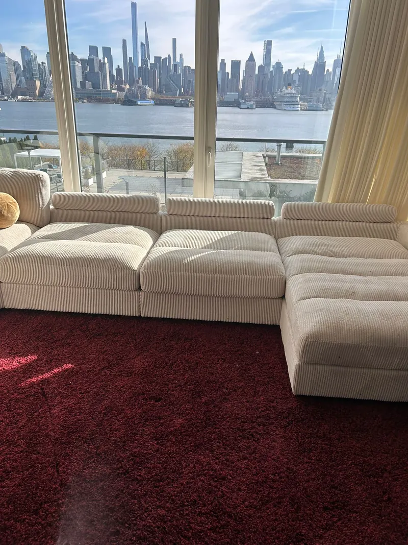 A cream sectional sofa on a red carpet in a living room with the Manhattan skyline across the river
