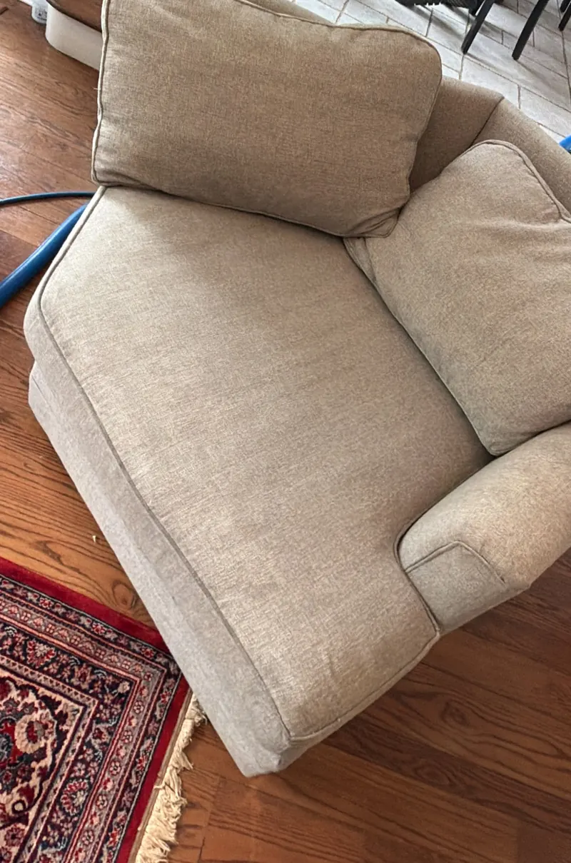 A beige fabric chaise sofa with a cleaning hose behind it